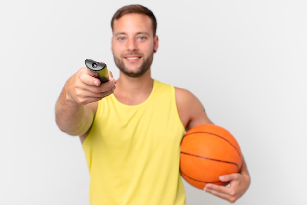 Hombre guapo con una pelota de baloncesto y elegir un canal con un controlador