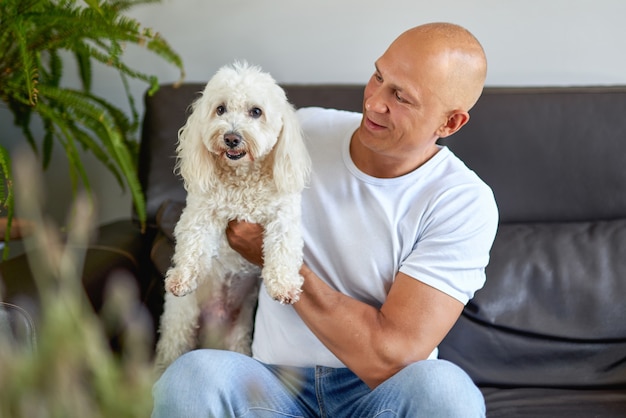 Hombre guapo con perro blanco en casa en el sofá