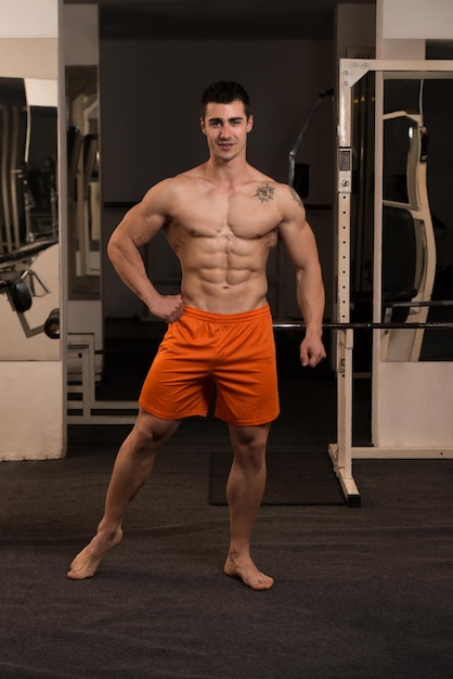 Hombre guapo de pie fuerte en el gimnasio y flexionando los músculos Muscular culturista atlético modelo de fitness posando después de los ejercicios