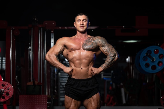 Hombre guapo de pie fuerte en el gimnasio y flexionando los músculos Muscular culturista atlético modelo de fitness posando después de los ejercicios