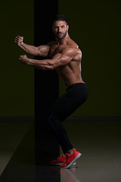 Hombre guapo de pie fuerte en el gimnasio y flexionando los músculos Muscular culturista atlético modelo de fitness posando después de los ejercicios