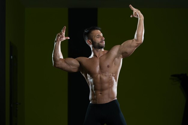 Hombre guapo de pie fuerte en el gimnasio y flexionando los músculos Muscular culturista atlético modelo de fitness posando después de los ejercicios