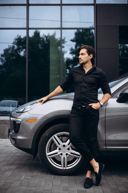 Hombre guapo de pie junto a su auto nuevo