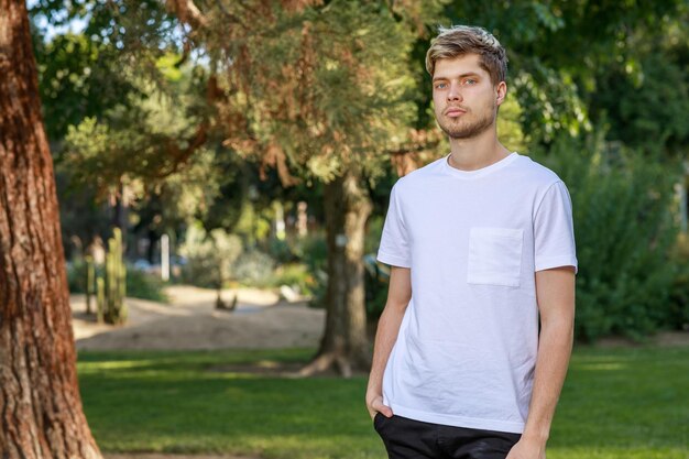 Hombre guapo de pie en el parque y mirando a la cámara