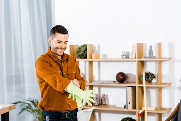 Hombre guapo de pie en la sala de estar moderna y poniéndose guantes de goma