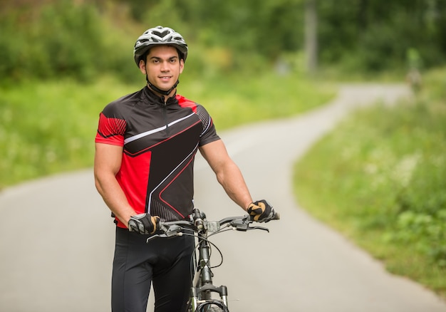 Hombre guapo de pie con su bicicleta en el camino forestal.