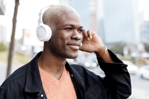 Hombre guapo con piel negra escucha la música en auriculares al aire libre