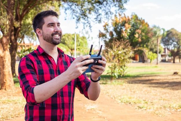 Hombre guapo en la plaza pilotando un dron. Chico joven con el control remoto filmando con el dron.