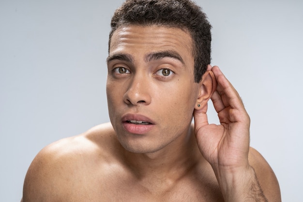 Hombre guapo poniendo su mano en la oreja