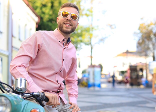 Hombre guapo posando en un scooter en un contexto de vacaciones. Moda y estilo de calle.