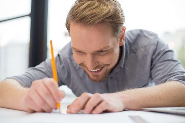 Hombre guapo positivo feliz sosteniendo un lápiz y tomando notas mientras tiene una nueva idea