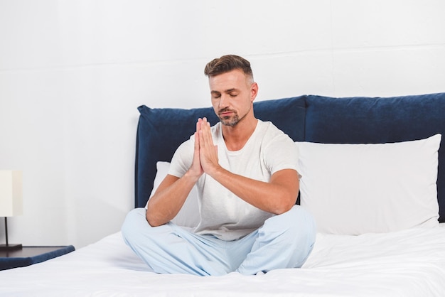 Hombre guapo practicando yoga en la cama