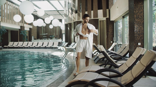 Foto hombre guapo quitándose la ropa cerca de la piscina de agua en el hotel de lujo