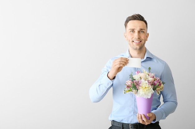 Hombre guapo con ramo de flores hermosas y tarjeta de felicitación