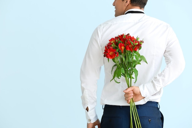 Hombre guapo con ramo de flores sobre fondo de color