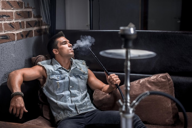 Un hombre guapo se relaja en un narguile en el bar. Concepto de tiempo agradable para pasar.