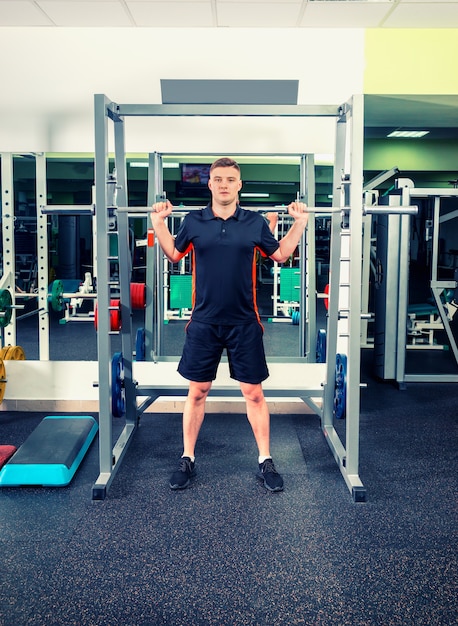 Hombre guapo en ropa deportiva levantando pesas mirando concentrado, trabajando en un gimnasio