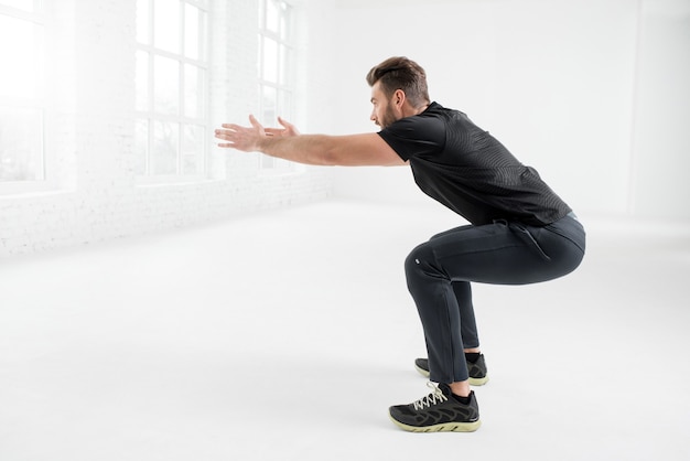 Hombre guapo en ropa deportiva negra con tablón en el interior del gimnasio blanco