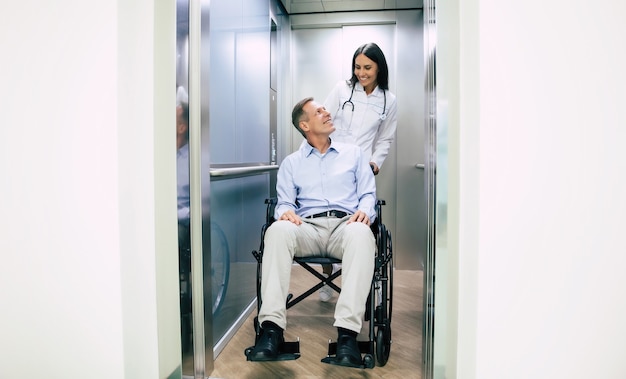 Hombre guapo senior en silla de ruedas se mueve en el hospital con la ayuda de personal médico especial