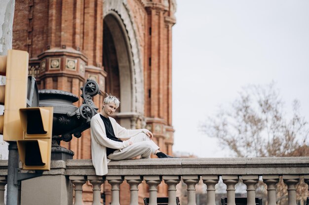 Hombre guapo sentado en la cerca cerca de un hermoso edificio antiguo