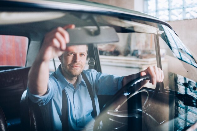 Foto hombre guapo sentado dentro de su auto antiguo