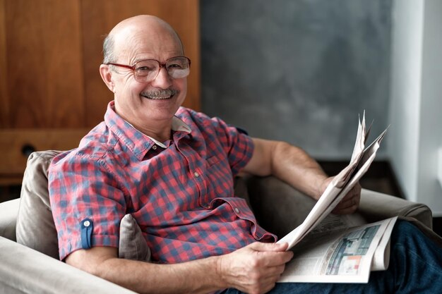 Foto hombre guapo sentado en la sala de estar leyendo el periódico sonriendo