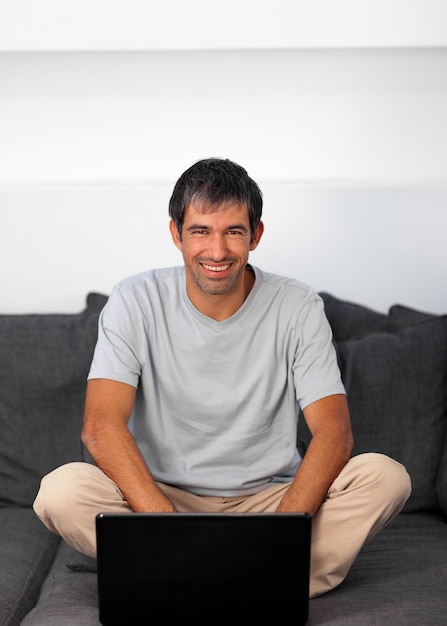 Hombre guapo sentado en el sofá con una computadora portátil