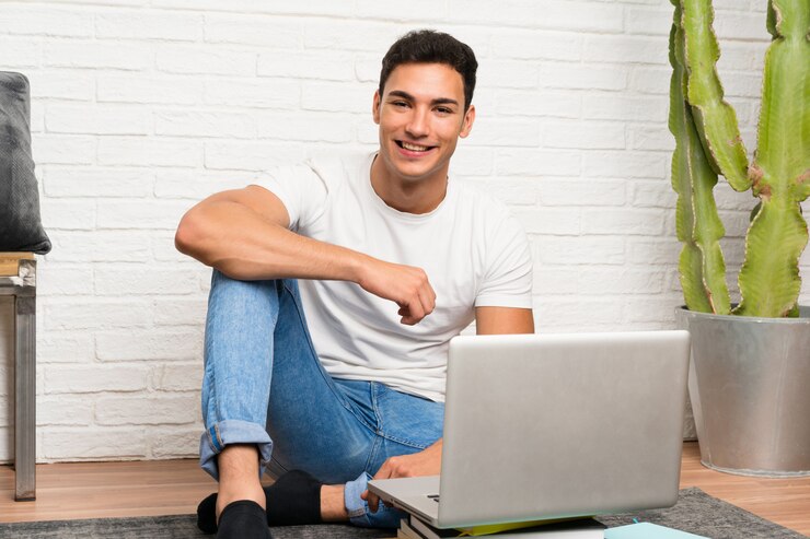 Foto hombre guapo sentado en el suelo con su computadora portátil