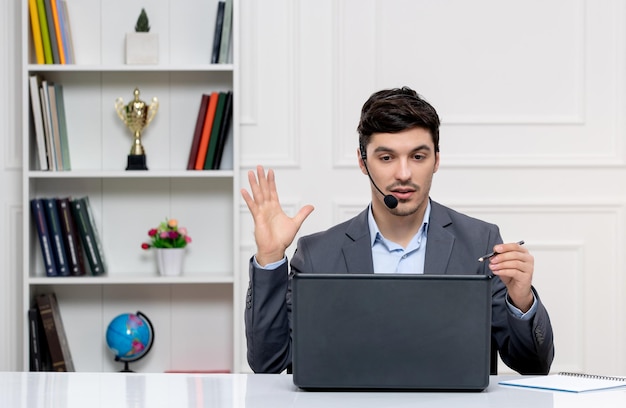 Hombre guapo de servicio al cliente en traje gris con computadora y auriculares con una pluma