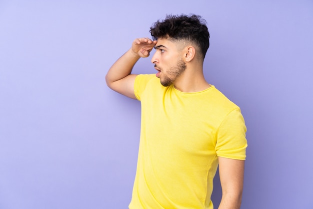 Hombre guapo sobre pared aislada con expresión de sorpresa mientras mira hacia el lado