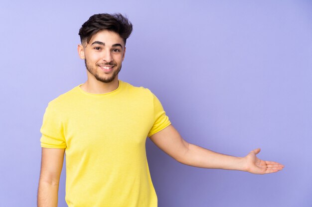 Hombre guapo sobre pared aislada extendiendo las manos a un lado para invitar a venir