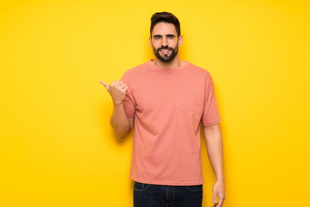 Hombre guapo sobre pared amarilla apuntando hacia el lado para presentar un producto