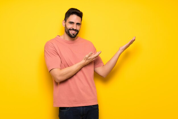 Hombre guapo sobre una pared amarilla que extiende las manos hacia el lado para invitar a venir