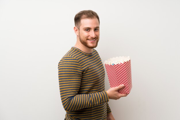 Hombre guapo sobre pared blanca aislada sosteniendo un tazón de palomitas de maíz