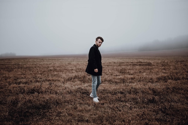 hombre guapo solitario en un abrigo negro en otoño en un campo