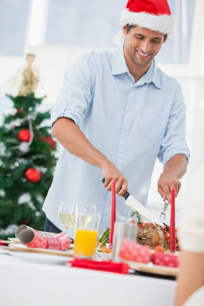 Hombre guapo con un sombrero de santa y tallar pollo asado en una cena de Navidad