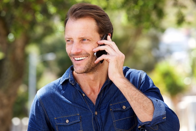 Hombre guapo sonriendo con teléfono móvil al aire libre