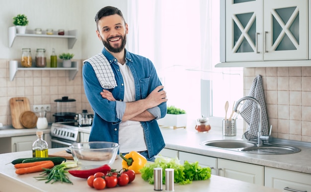 Hombre guapo sonriente barbudo en la cocina en casa está planteando y