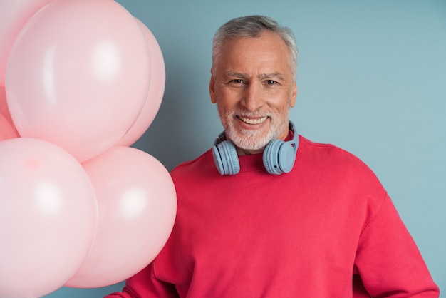 Hombre guapo y sonriente con cabello gris usa auriculares, sosteniendo globos.