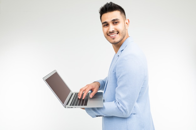 Hombre guapo sonriente en una chaqueta azul con una computadora portátil abierta en sus manos sobre un fondo blanco de estudio