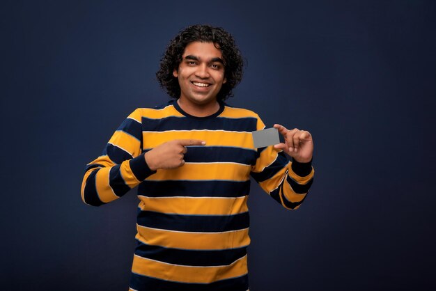 Hombre guapo sonriente joven posando con una tarjeta de crédito o débito sobre fondo gris