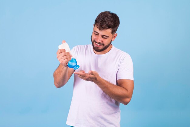 Hombre guapo sonriente poniéndose protector solar sobre fondo azul con espacio libre para texto Cuidado de verano y vacaciones