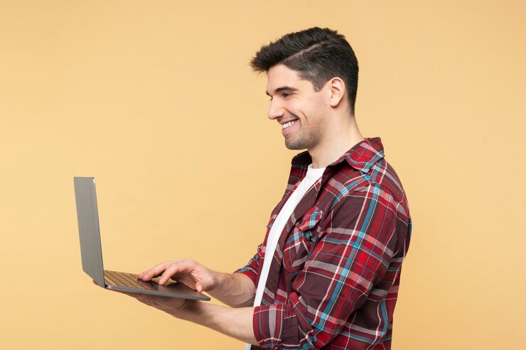 Foto hombre guapo sonriente usando una computadora portátil escribiendo en un teclado posando aislado en un fondo amarillo