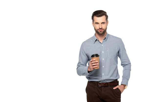 Hombre guapo sosteniendo café para llevar y de pie con la mano en el bolsillo aislado en blanco