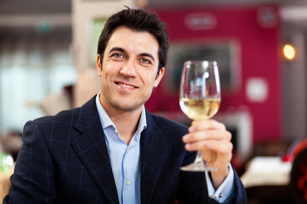 Hombre guapo sosteniendo una copa de vino blanco en el restaurante