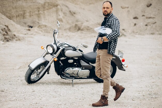 Hombre guapo con su moto en cantera de arena