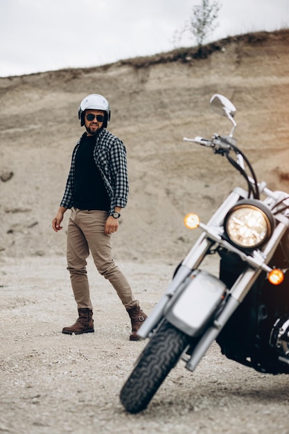 Hombre guapo con su moto en cantera de arena