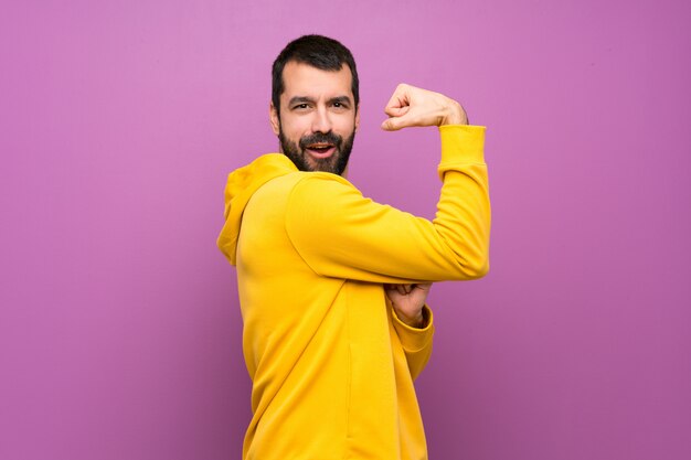 Foto hombre guapo con sudadera amarilla haciendo gesto fuerte
