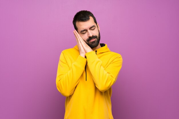 Hombre guapo con sudadera amarilla haciendo gesto de sueño en expresión dorable