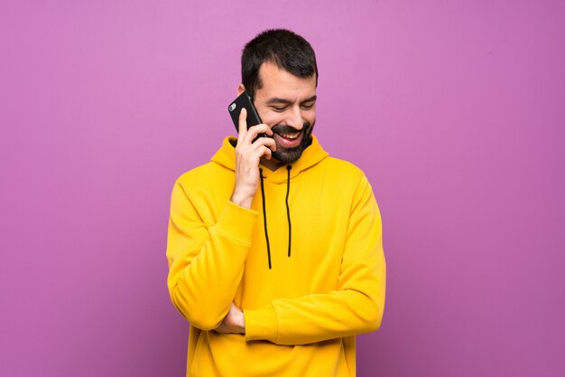 Hombre guapo con sudadera amarilla manteniendo una conversación con el teléfono móvil